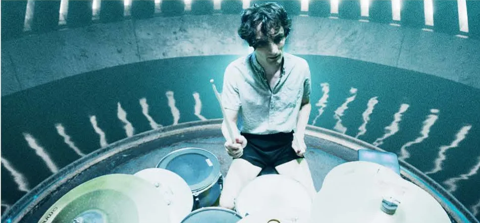 A drummer seen from above, lit in hue-shifted cyan.